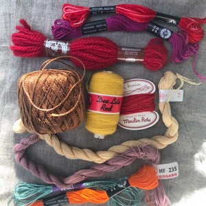 May include: Assortment of embroidery floss and yarn in various colors, including red, orange, yellow, brown, purple, and teal. The yarn is wound into balls and skeins, and some of the floss is labeled with the brand name "Moulin&eacute;" and the color number "28".