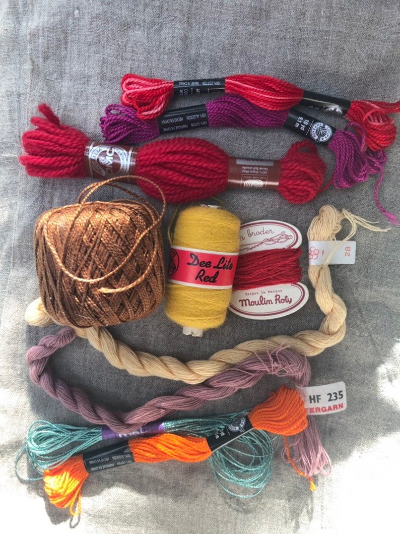 May include: Assortment of embroidery floss and yarn in various colors, including red, orange, yellow, brown, purple, and teal. The yarn is wound into balls and skeins, and some of the floss is labeled with the brand name "Moulin&eacute;" and the color number "28".