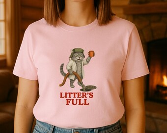 以下が含まれることがあります： ピンク色のTシャツ。下水作業員に扮した漫画の猫が、コーヒーカップとホースを持っています。「LITTER'S FULL」の文字が赤色で猫のイラストの下にプリントされています。猫は帽子と白いコートを着ています。