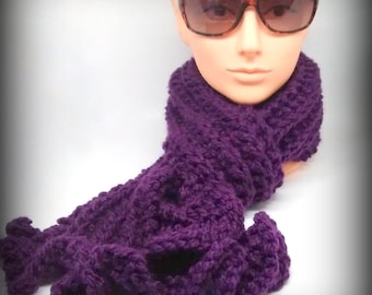 May include: A purple knitted scarf with a ruffled design. The scarf is draped around a mannequin wearing sunglasses.