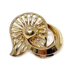 May include: Gold-toned vintage brooch with a unique design. The brooch features a central sphere, a fan-shaped element with radiating lines, and a curved, looped accent. The piece is set against a white background.