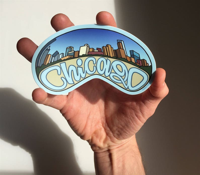 Op de afbeelding: Een blauwe en witte sticker met een stadsbeeld en het woord "Chicago" in een gestileerd lettertype.