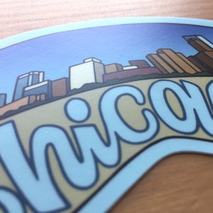 Op de afbeelding: Een blauwe en witte sticker met een gestileerde skyline en het woord "Chicago" in een blauw lettertype.