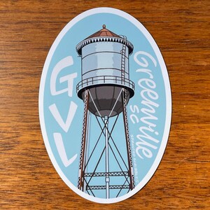 May include: A blue and white oval sticker featuring a drawing of a water tower and the text "GVL Greenville SC" in a white cursive font.