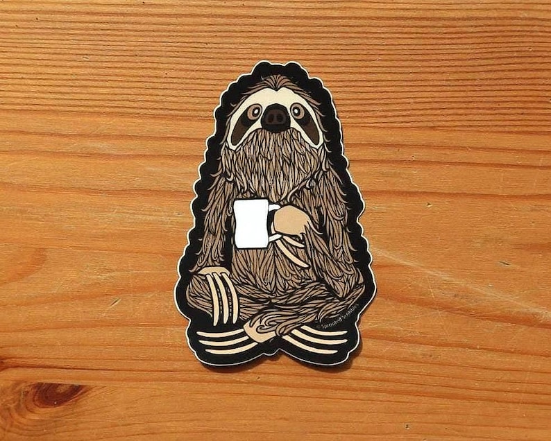 May include: A die-cut sticker featuring a brown, furry sloth sitting in a cross-legged position. The sloth has dark markings around its eyes and is holding a plain white mug with both hands. The illustration has a thick black border outline.
