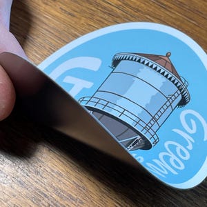 May include: A blue and white round sticker featuring a water tower illustration and the word "Crown" written in white cursive.