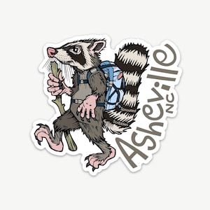 May include: A die-cut sticker featuring a cartoon raccoon wearing a blue backpack and holding a wooden walking stick. The raccoon has grey fur, a striped tail, and pink paws. The text Asheville NC and Sprouted Scribbles is printed.