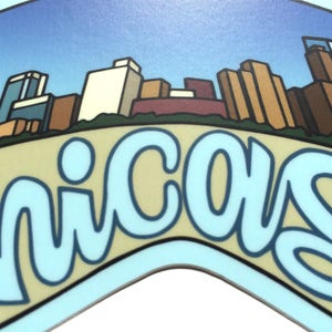 Op de afbeelding: Een blauwe en witte sticker met een gestileerde afbeelding van de skyline van Chicago en het woord "Chicago" in een blauw lettertype.