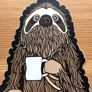 Puede incluir: Un perezoso marr&oacute;n y negro sosteniendo una taza blanca. El perezoso tiene un dise&ntilde;o detallado y estampado.