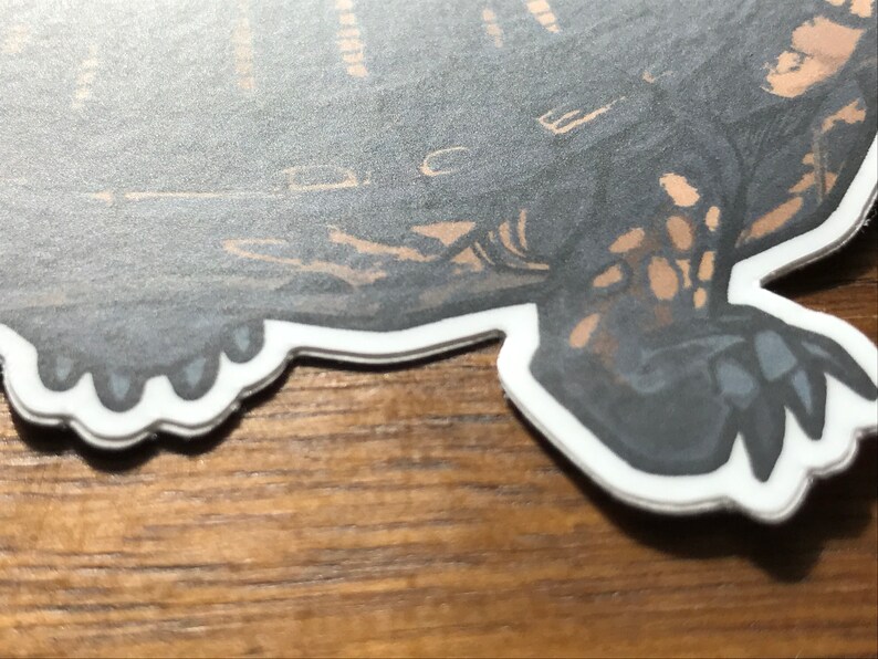 May include: A die-cut sticker featuring a detailed illustration of a turtle with a dark gray shell and tan markings. The turtle has visible claws on its feet and is outlined with a thick white border, showcasing a high-contrast graphic design.