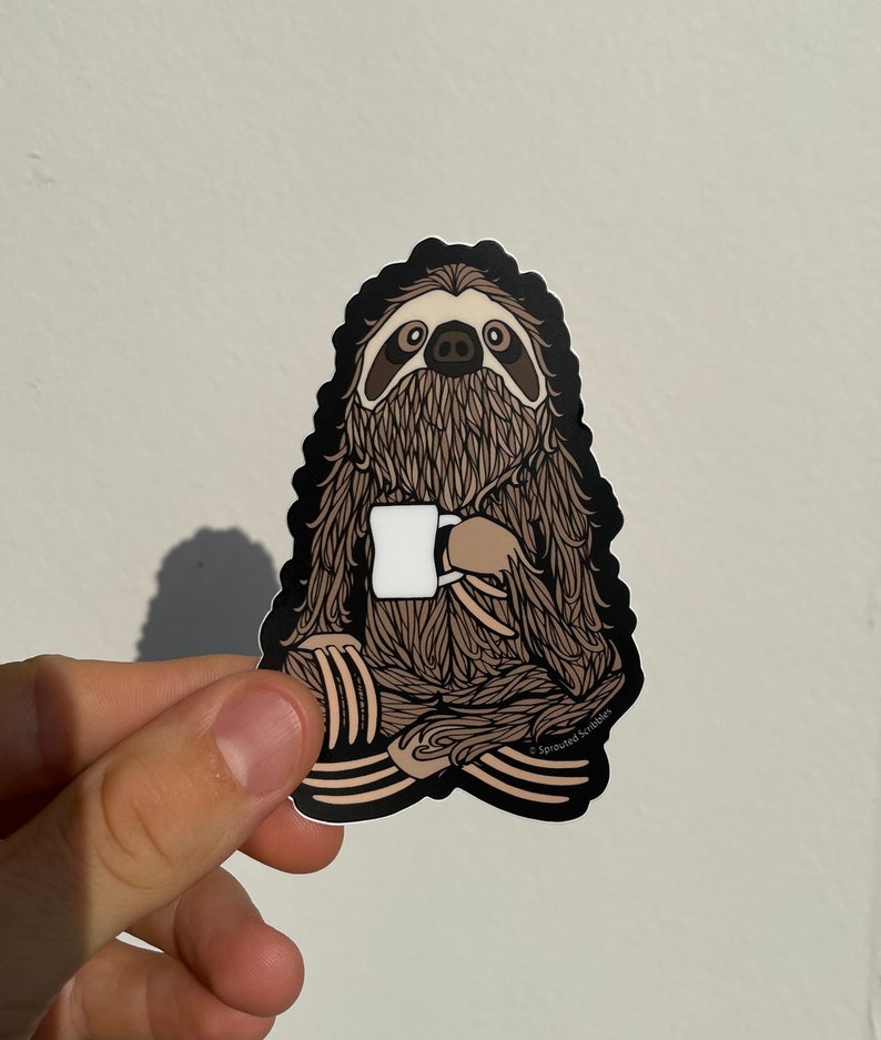 Puede incluir: Una pegatina negra y marr&oacute;n con un perezoso de dibujos animados sosteniendo una taza blanca. El perezoso est&aacute; sentado en una postura relajada con las piernas cruzadas. La pegatina tiene el texto "Sprouted Scribbles" en la esquina inferior derecha.