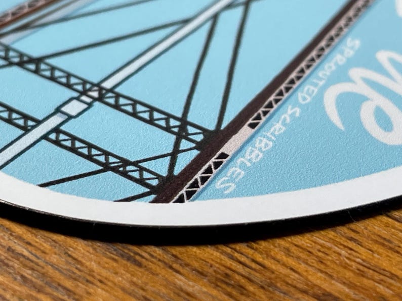 May include: A blue and white round sticker with a black and white illustration of a bridge. The sticker has the text "Spotted Squirrel" written on it.