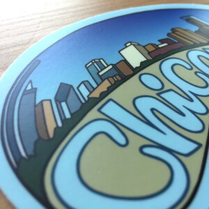 Op de afbeelding: Een blauwe en witte sticker met een skyline van gebouwen en het woord "Chicago" in een gestileerd lettertype.