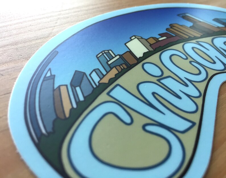 Op de afbeelding: Een blauwe en witte sticker met een skyline van gebouwen en het woord "Chicago" in een gestileerd lettertype.