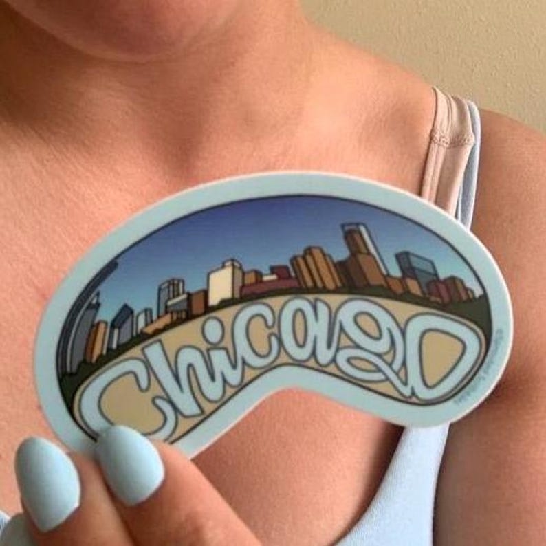 Op de afbeelding: Een blauwe en witte sticker met een stadsbeeld en het woord "Chicago" in een gebogen lettertype.