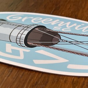 May include: A blue and white oval sticker with a drawing of a water tower and the text "Greenville SC" in a white cursive font.