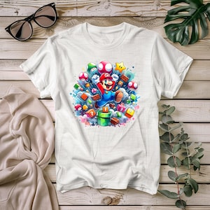 Peut inclure: T-shirt blanc avec un graphisme coloré de Mario sautant au milieu d'éléments de jeu. Le motif comprend des champignons, des étoiles et des blocs avec des points d'interrogation, sur fond d'aquarelle. Un design amusant et vibrant.
