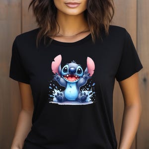 Könnte beinhalten: Schwarzes T-Shirt mit einer Cartoon-Illustration von Stitch, einem blauen Alien mit großen Ohren und einem breiten Lächeln. Die Grafik enthält Wasserspritzer. Das T-Shirt ist aus weichem Material.