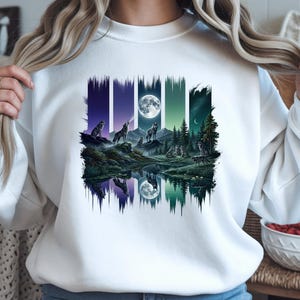 May include: White sweatshirt with a colourful graphic depicting wolves howling under a full moon. The design shows a forest scene with a full moon reflected in the water, in shades of blue, green, and purple.