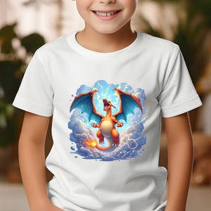 May include: White t-shirt with a colourful cartoon dragon design. The dragon has orange and red scales, blue wings, and a fiery tail, set against a background of clouds and lightning. The shirt is worn by a child.