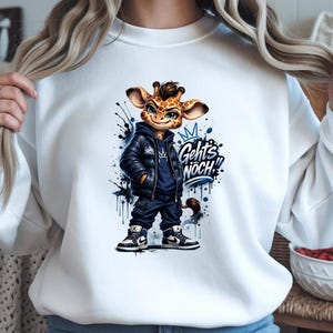 Può includere: Felpa bianca con una giraffa dei cartoni animati con giacca di pelle nera, felpa con cappuccio blu e scarpe da ginnastica. La giraffa ha una corona e la scritta "Geht's NOCH!!" in blu. Dettagli di vernice blu e nera completano il design.