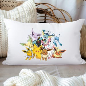 Op de afbeelding: Wit rechthoekig kussen met een kleurrijke afbeelding van verschillende stripfiguren. De karakters zijn in tinten geel, roze, blauw en zwart. Het kussen ligt op een oppervlak met andere kussens en decoratieve elementen.