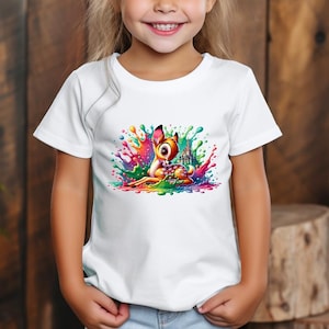 Op de afbeelding: Wit T-shirt met een kleurrijke afbeelding van een cartoon hert en kasteel. Het hert is omringd door verfspatten in roze, blauw, groen en geel. Het shirt wordt door een kind gedragen.