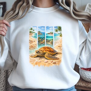 May include: White sweatshirt with a vibrant print of a sea turtle on a beach scene. The design showcases a turtle, sandy shore, and a tropical ocean with palm trees, evoking a coastal aesthetic.