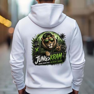 Peut inclure: Sweat à capuche blanc avec un motif de lion portant des lunettes de soleil et une casquette, avec un skateboard et un boombox. Le design comprend le texte "JUNGS KRAM" en vert et noir.