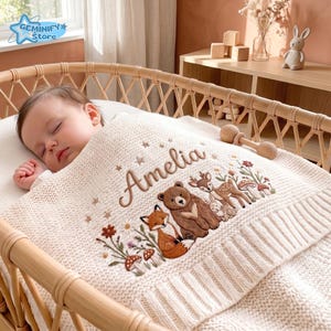 Pu&ograve; includere: Una coperta per neonati in maglia color crema con un ricamo raffigurante una volpe, un orso, un cervo e un coniglio circondati da fiori e funghi. Il nome Amelia &egrave; ricamato in corsivo marrone sopra gli animali, con piccole stelle decorative.