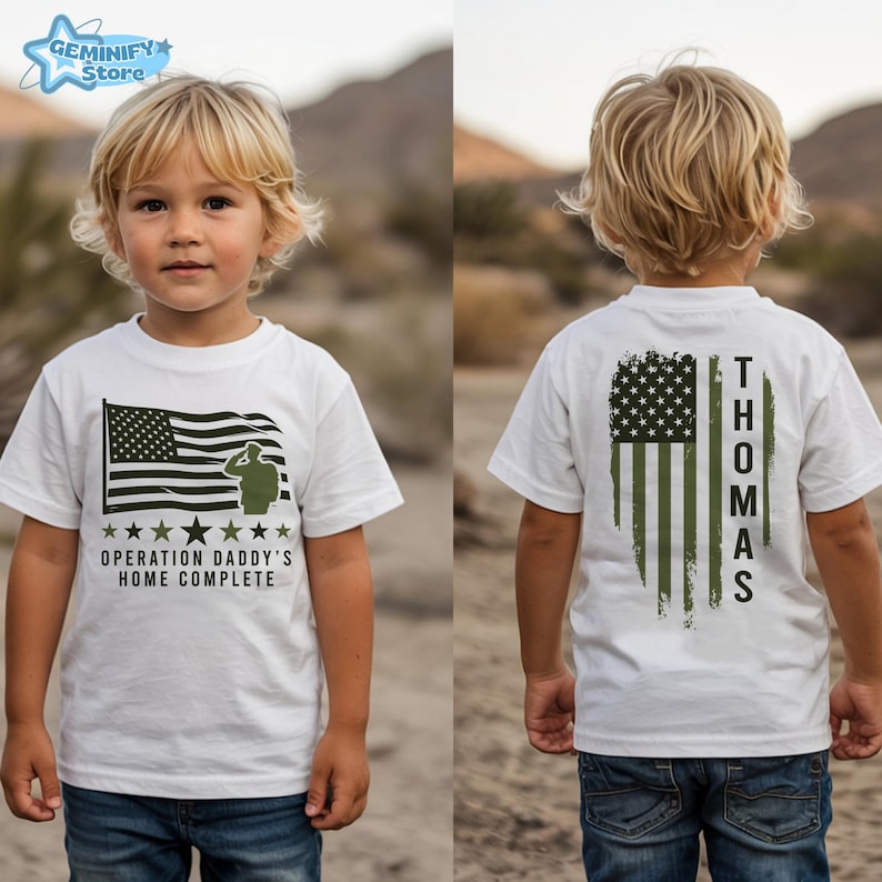 May include: White t-shirt featuring an American flag design with the text "OPERATION DADDY'S HOME COMPLETE" on the front. The back of the shirt displays a distressed American flag with the name "THOMAS" printed vertically.