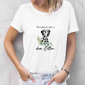 May include: White t-shirt featuring a Dalmatian dog illustration with black spots, surrounded by green leaves. The shirt has the text "Too glam to give a damn...cation."