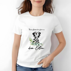 May include: White t-shirt featuring a Dalmatian dog illustration with black spots and green foliage. The text reads "Too glam to give a damn...cation."