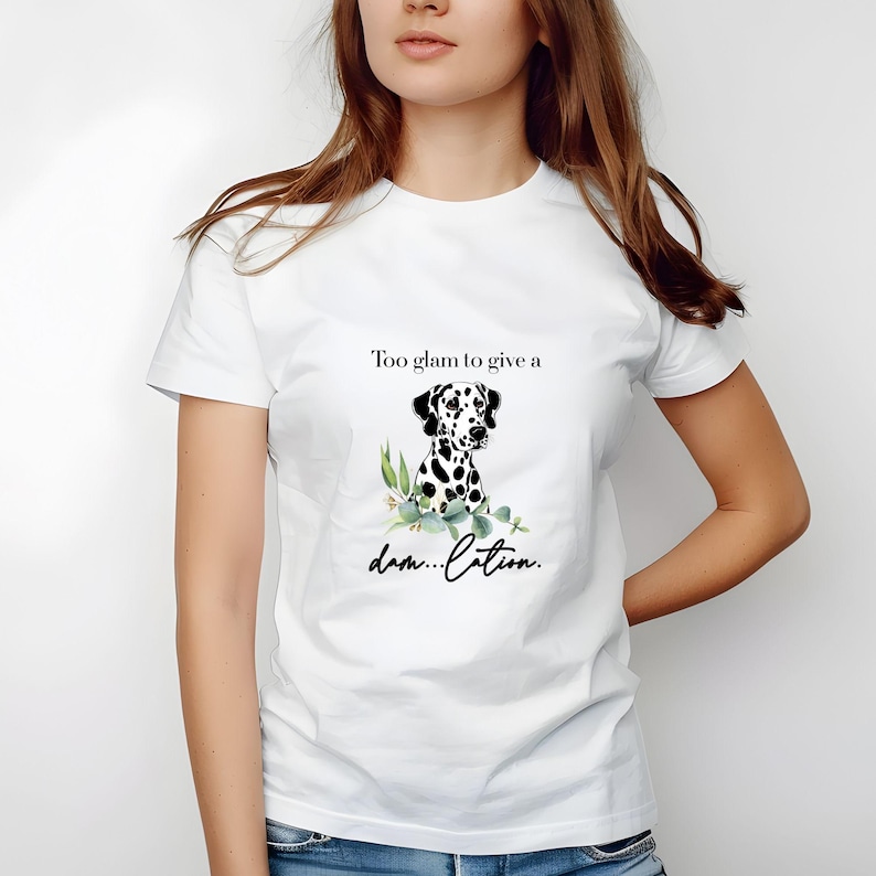 May include: White t-shirt featuring a Dalmatian dog illustration with black spots and green foliage. The text "Too glam to give a dam...lation" is printed above and below the dog graphic.