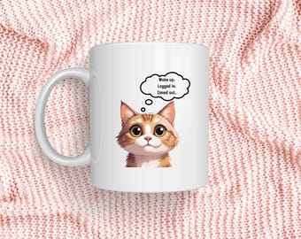 May include: White ceramic mug featuring a cartoon cat with large eyes and orange and brown fur. A thought bubble above the cat's head reads, "Wake up. Logged in. Zoned out." The mug has a curved handle and is set against a pink knitted background.