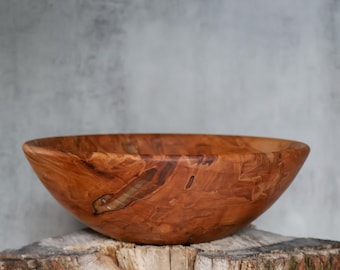 May include: A round wooden bowl with a smooth, polished finish, showcasing a rich, warm brown color with prominent natural wood grain patterns, swirls, and dark knots throughout the surface, featuring a wide, open top and a curved, deep basin.