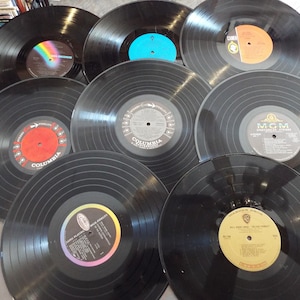 May include: A collection of black vinyl records with various label designs. Some labels are red, orange, blue, and white. The records are arranged in a circular pattern, showcasing the variety of music.