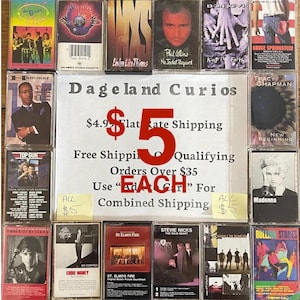May include: A collection of vintage cassette tapes featuring various music artists and albums. The tapes are displayed on a wooden surface, with a sign that reads "Dageland Curios". The image includes text such as "Each" and "All $5".