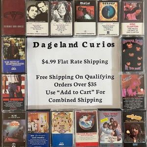 May include: A collection of vintage cassette tapes featuring various artists, including Tom Petty, Bruce Springsteen, Eric Clapton, and The Who. The tapes are displayed on a shelf with a sign that reads "Dageland Curios" and includes information about shipping rates.