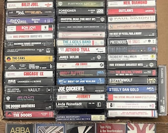May include: A collection of music cassette tapes arranged in a box, featuring various artists including Aerosmith, The Beatles, Billy Joel, Bon Jovi, Elton John, Fleetwood Mac, Grateful Dead, ABBA, and Tom Petty and the Heartbreakers.