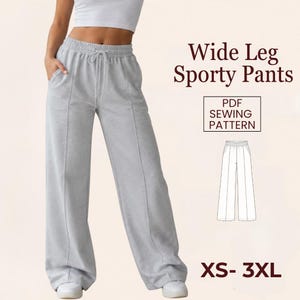 Op de afbeelding: Lichtgrijze sportbroek met wijde pijpen, een taille met trekkoord en zakken. De afbeelding bevat de tekst "Wide Leg Sporty Pants", "PDF Sewing Pattern" en "XS-3XL". De broek wordt door een persoon gedragen.