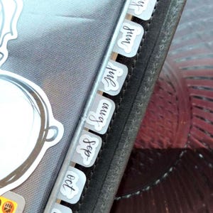 May include: A gray planner with month tabs labeled May, Jun, Jul, Aug, Sep, Oct, and Nov. The tabs are white with black handwritten font. A sticker is visible on the planner's cover.