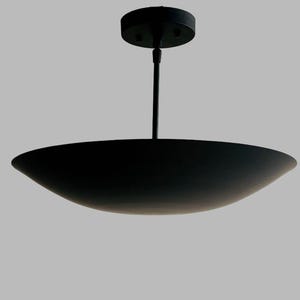 May include: A modern, black ceiling light fixture. The light has a circular base that attaches to the ceiling, a slender rod, and a wide, shallow, bowl-shaped shade. The fixture is suspended against a neutral gray background.