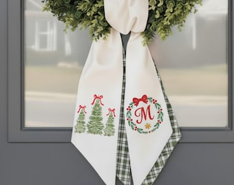 May include: White Christmas door hanger with green and red accents. The door hanger features a green wreath and a white ribbon with Christmas tree and wreath designs. The wreath design includes the letter "M".