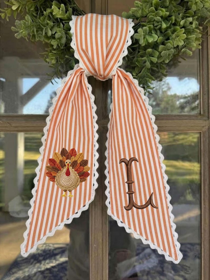 May include: A decorative fabric door hanger featuring orange and white vertical stripes with white scalloped lace trim. One side displays an embroidered turkey with colorful feathers, while the other side features a large, brown embroidered letter L.