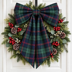 May include: A holiday wreath featuring a large fabric bow with a dark green, navy blue, and red plaid pattern. The wreath is constructed from evergreen branches, pinecones, and clusters of bright red berries, accented with small green leaves.
