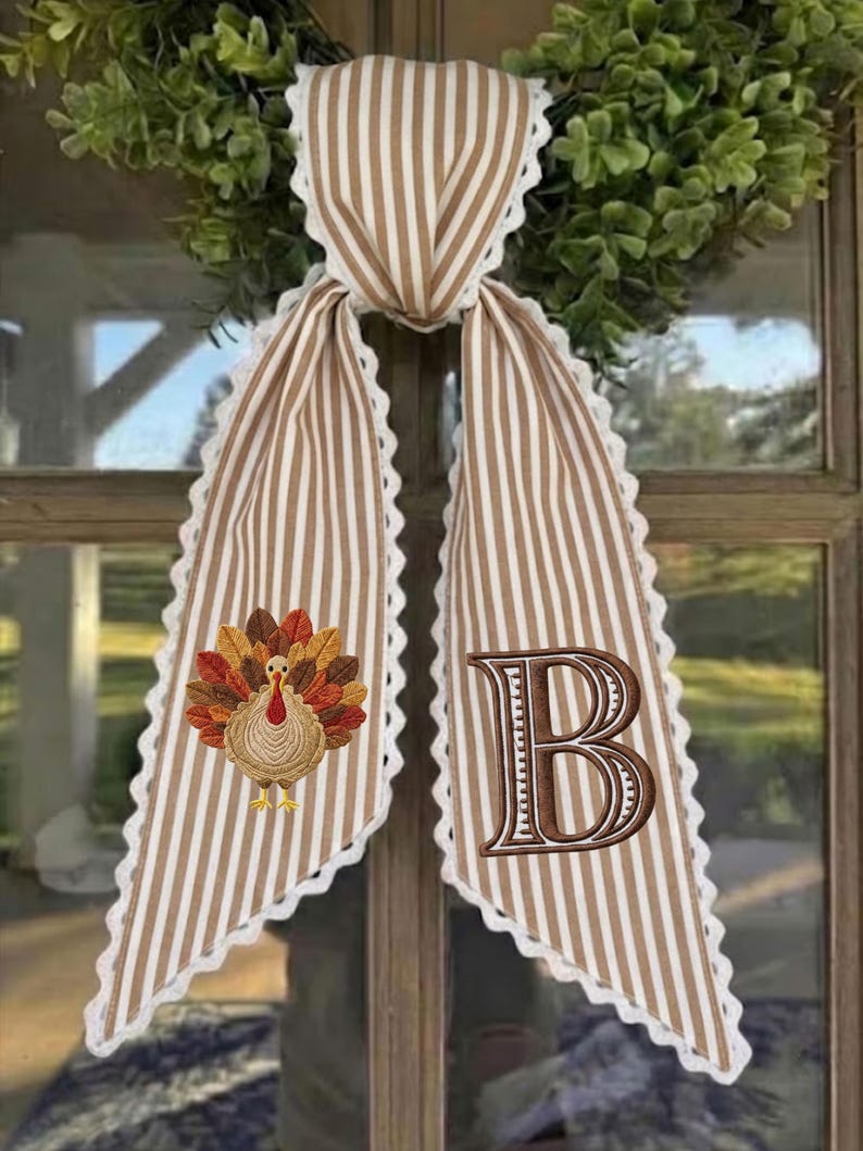 May include: A decorative fabric door hanger featuring a tan and white vertical striped pattern with white scalloped lace trim. One side displays an embroidered turkey with colorful feathers, while the other side features a large embroidered letter B.