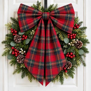 May include: A circular wreath made of green pine branches, decorated with clusters of red berries, small white berries, and brown pinecones. A large, prominent bow made of red, green, and yellow plaid fabric is attached to the top center.