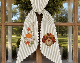 May include: A long, light green and white striped fabric ribbon with scalloped edges. One side features an embroidered design of orange and white pumpkins with autumn leaves, while the other side displays an embroidered turkey with colorful feathers.