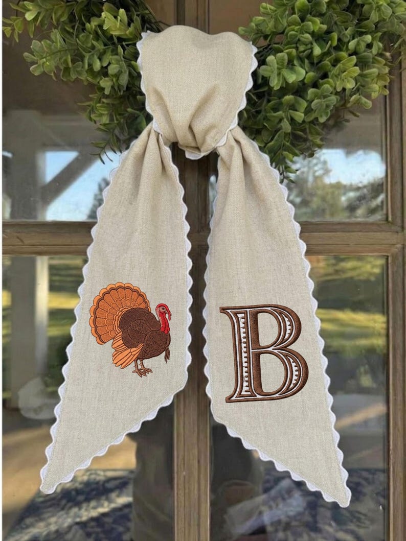 May include: A beige linen-like fabric door hanger featuring a scalloped white edge. One side displays an embroidered brown and orange turkey, while the other side features a large, embroidered brown letter B with white detailing.